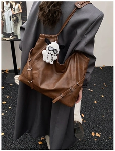 Brown leather tote bag with a pilot plush charm and metallic buckle detail shown on shoulder