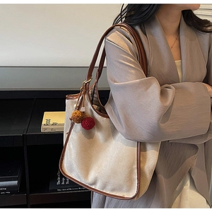 Détail du sac cabas en toile beige avec bordure en cuir marron et pompons colorés