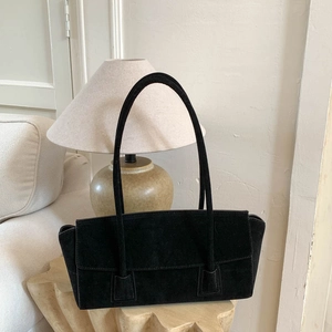 Détail d'un sac cabas en daim noir avec doubles lanières sur socle en bois naturel