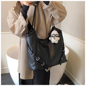 Detail of black faux leather tote bag with silver buckles and a white plush dog charm