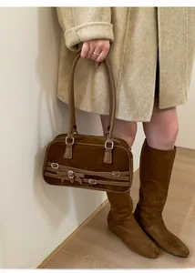 Close-up of brown suede bowling bag with silver buckles worn with a beige coat