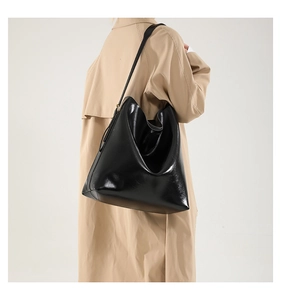 Detailansicht einer großen schwarzen Leder-Tote-Bag mit breiten Riemen auf einem khakifarbenen Mantel