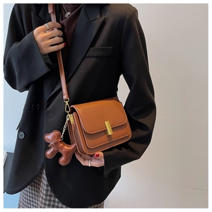Vue détaillée du sac à bandoulière en cuir marron avec boucle dorée et breloque chien sur modèle