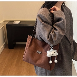 Brown suede tote bag with braided handle and plush charm shown on a grey blazer outfit