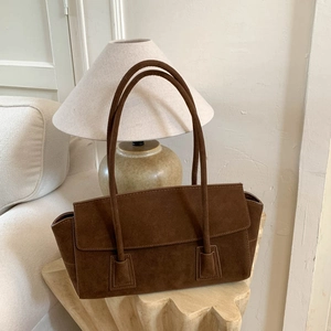 Détail d'un sac cabas en daim marron foncé posé sur une table en bois dans une pièce