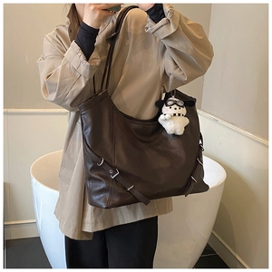 Detail view of dark brown faux leather tote with silver metal buckles and dog plush charm
