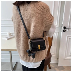 Détail d'un sac carré noir avec fermoir doré et pendentif de chien en ballon
