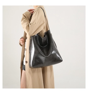Seitenansicht der großen, glänzenden Ledertasche am Modell mit khakifarbenem Trenchcoat