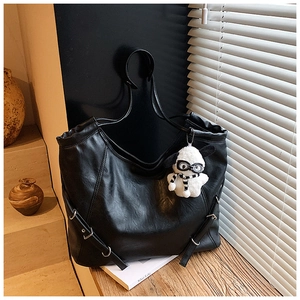 Detail shot of black faux leather tote bag with silver buckles and a cute plush puppy pendant