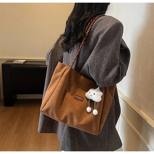 Detail of brown suede tote bag with leather label and white cloud plush charm
