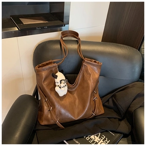 Brown faux leather tote bag with plush puppy pendant on a black leather sofa