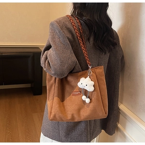 Detail of tan suede tote bag with woven shoulder strap and cute cloud charm accessory