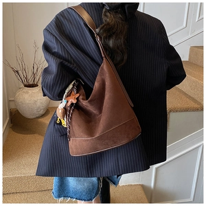 Brown suede tote bag detail with star and bear charms worn by a model on stairs