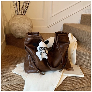 Close-up of a large brown leather tote bag with a cute plush dog pendant on stairs