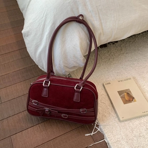 Close-up of burgundy suede bowling bag with bow details on a white bed background