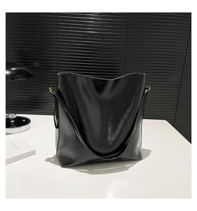 Detailansicht der glänzenden schwarzen Ledertasche mit goldener Metallschnalle und Textur