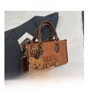 Détail du sac à main marron en cuir texturé avec lettrage embossé et pendentif ours