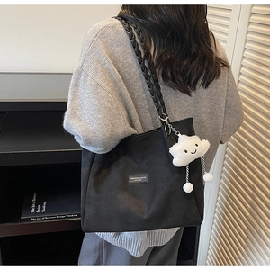 Close-up of black tote bag with woven strap and a cute white plush cloud charm detail