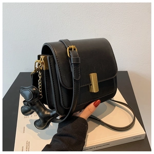 Détail du sac carré noir mat avec fermoir doré, plis accordéon et breloque chien
