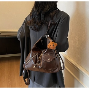 Detail of dark coffee leather hobo bag with metal zippers and a plush bear charm