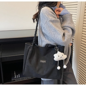 Close-up of black tote bag with woven straps and a white cloud plush charm pendant