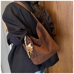 Detail of a large brown suede tote bag featuring a cute teddy bear plush charm
