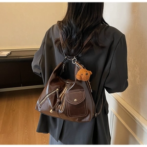 Detail view of deep brown faux leather backpack with plush bear charm decoration