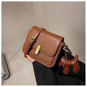 Détail d'un sac bandoulière marron avec boucle dorée et pendentif chien design