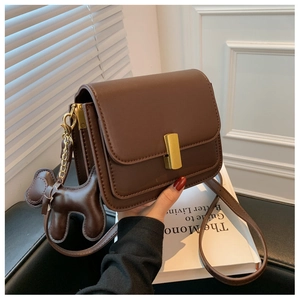 Détail du sac bandoulière en cuir marron foncé avec boucle dorée et breloque chien