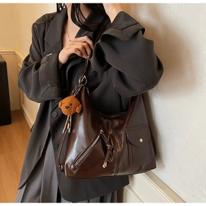 Detail view of deep brown oily leather tote bag with decorative zippers and plush bear charm