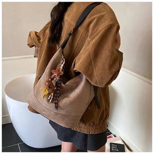 Detail of a brown suede bucket bag with black leather straps and star bear bag charms
