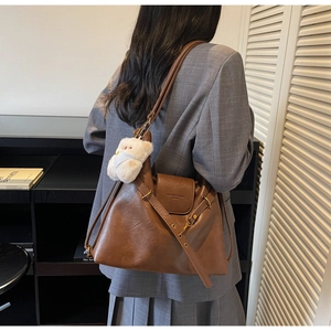 Close-up of brown vintage shoulder bag with textured leather and a white plush bear charm