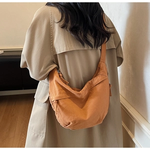 Rear view of a model wearing the large orange canvas crescent crossbody bag with a trench coat