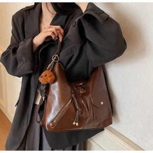Detail of dark brown leather tote bag with functional exterior pockets and teddy bear charm
