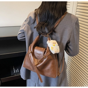 Close-up of vintage brown leather backpack with bear charm on grey plaid blazer