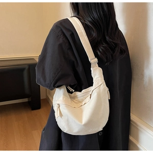 Minimalist cream canvas crossbody crescent bag worn by a model in a studio setting