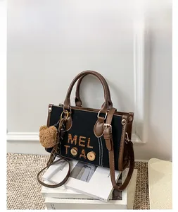 Détail du sac en toile noire avec lanières en cuir marron et pendentif ours en peluche