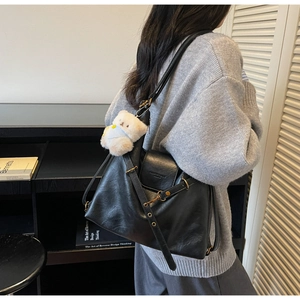 Detail view of black leather shoulder bag with cute white plush bear pendant and metal buckles