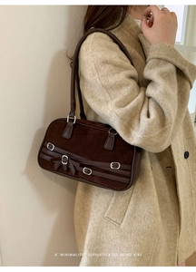 Close-up of retro brown suede shoulder bag with buckle and bow detail on beige coat