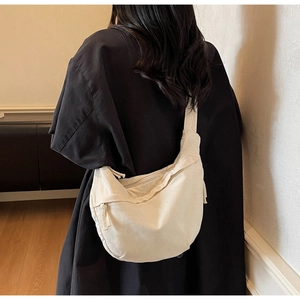 Minimalist cream white canvas crescent crossbody bag worn over a black oversize jacket