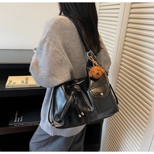 Close-up of black PU leather shoulder bag with silver zipper and brown bear pendant