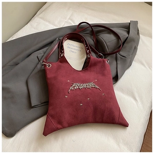 Detailed view of burgundy suede tote with gothic metal logo and silver stud decorations