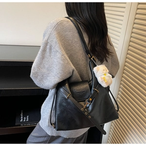 Detail of black faux leather tote bag with metal buckle and plush bear pendant