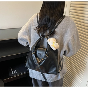 Detail of black leather backpack with gold metal hardware and white plush keychain pendant