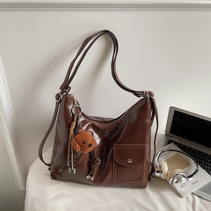 Close-up of brown shiny PU leather hobo bag with a plush bear charm on a desk