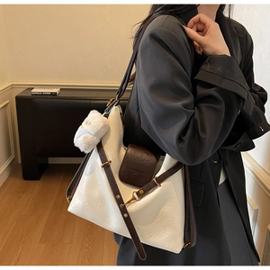 Detail of a large cream tote bag with brown trim and plush bear charm on a black blazer