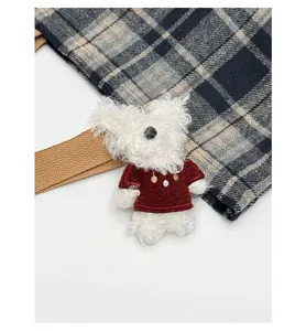 Close-up of white plush bear charm with burgundy knit sweater on plaid bag strap