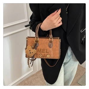 Détail d'un sac vintage marron avec lettrage MEL TOAO gaufré et un porte-clé ours en peluche