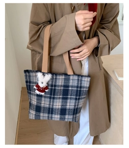 Detail of tweed checkered tote bag with a small rabbit plush pendant and shoulder strap