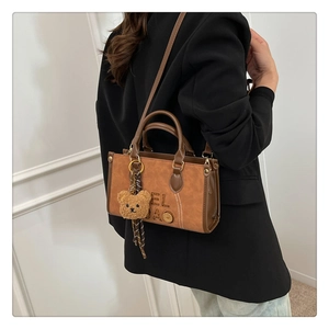 Gros plan d'un sac à main marron vintage avec logo embossé et détail de charm d'ours mignon